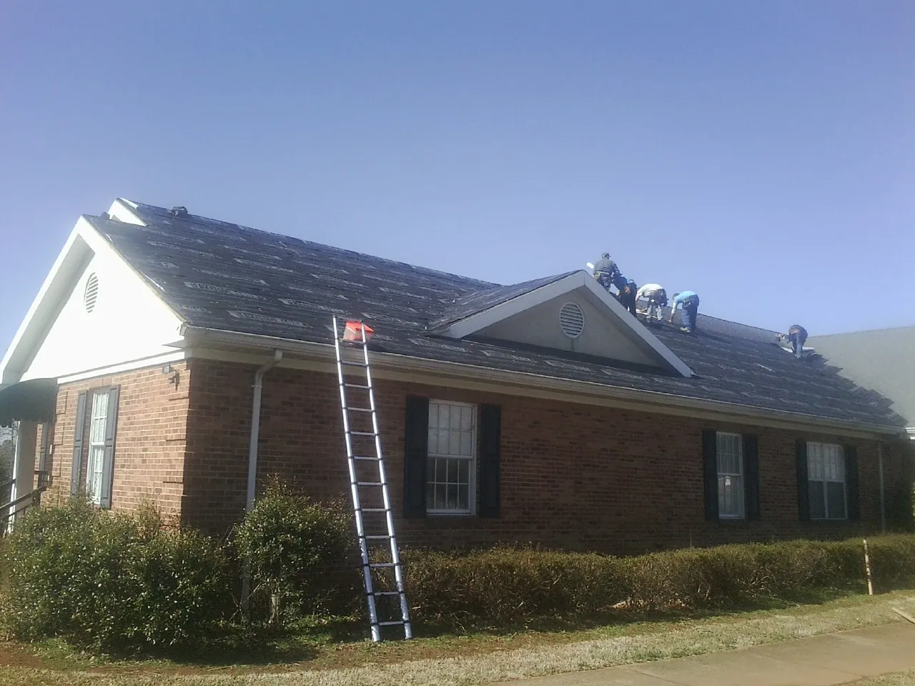 Crew tearing shingles off a brick ranch roof with a ladder set — Metal Roof Repair work by our crew in Bellingham