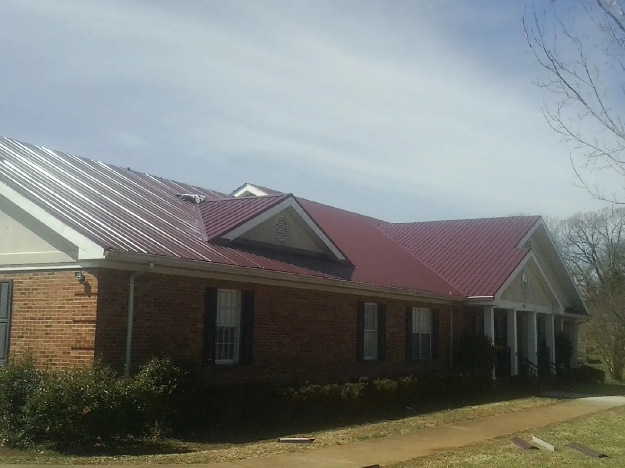 Red metal roof with gabled entries on a long brick building, from a Hail Damage Roof Repair job in Bellingham